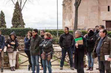 Fotografía de un grupo de personas oyendo la explicación de un guía turístico en los alrededores de una edificación histórica.